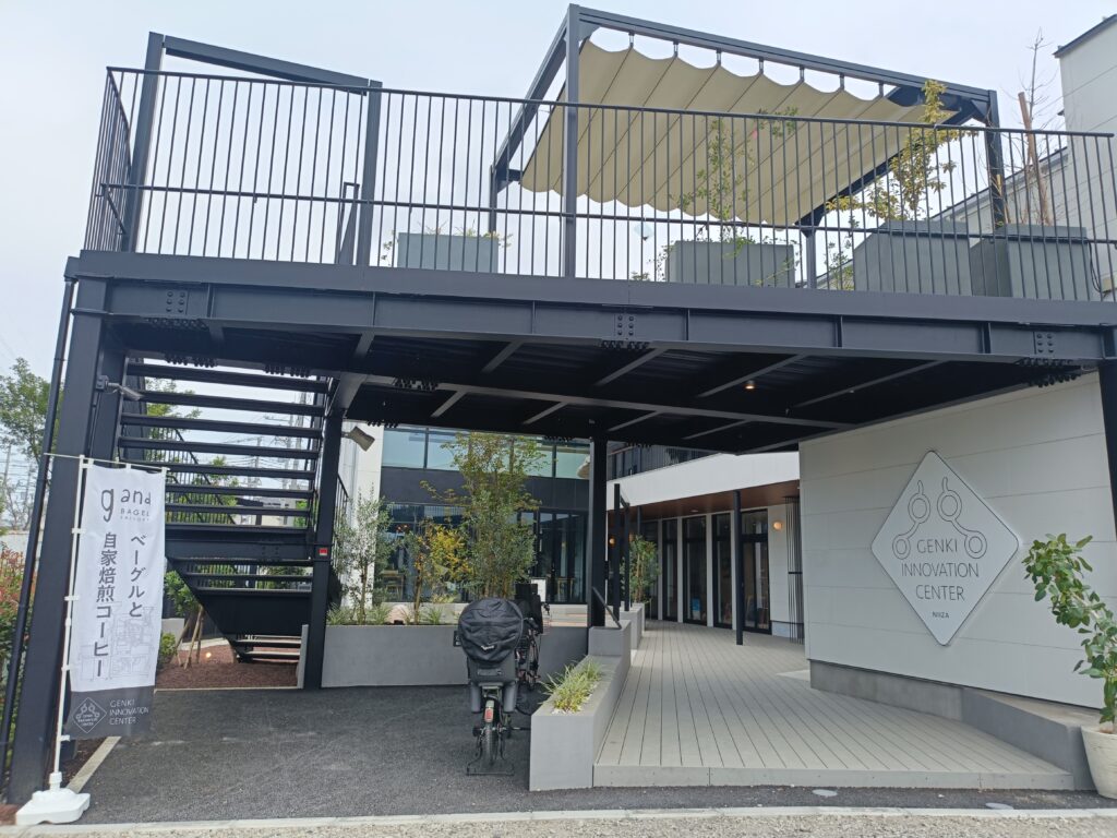 黒い鉄骨の建物「GENKI INNOVATION CENTER NIIZA」の入口。ベーグルと自家焙煎コーヒーののぼりが立つ